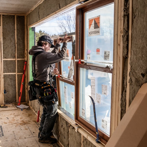 A man installs a window with Andersen stickers inside a new home build.